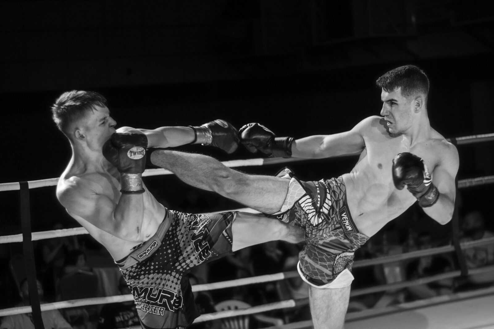Two skilled fighters exchange powerful kicks in an intense kickboxing match.
